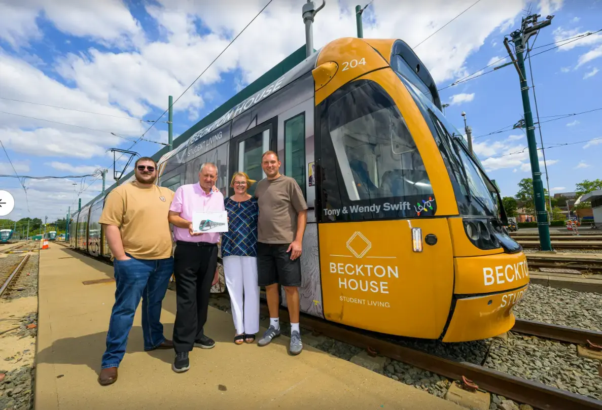 Tony and Wendy Swift stand with family members beside their newly named NET tram, holding a framed certificate to mark the honour.